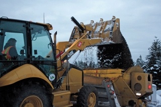 Kelli Short dumps sand into the back of a large county truck equipped with a plow.