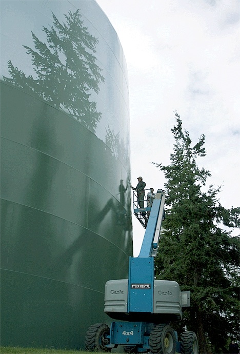 Two Hennig’s Mural Design employees paint an evergreen forest-scape on the larger of two water city storage tanks off Heller Road.