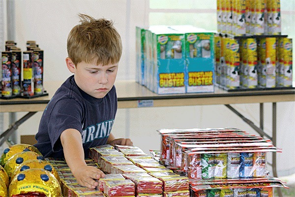 Six-year-old Logan Martin helps organize merchandise at the Phantom Fireworks stand in Coupeville.  People wanting to purchase and use personal fireworks must adhere to state time and place restrictions.