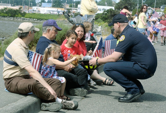 Kimberly and Ruby George snatch candy from a firefighter’s helmet during Monday’s parade in Oak Harbor. Their parents