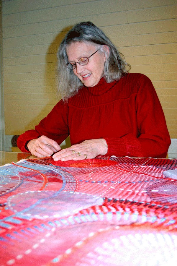 Marianne Burr hand stitches a quilt. At left and right are parts of her winning quilt