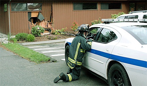 A Central Whidbey Fire and Rescue firefighter talks with a Coupeville deputy marshal after a medical office was damaged Thursday morning after an SUV crashed into it. Nobody was injured.