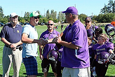 Oak Harbor Rotary Club President Aaron Syring (light shirt) shakes hands with Oak Harbor Youth Football League President Eric Marshall. The Rotary Club bought the local league new helmets this season. Former Rotary President Jim Bird