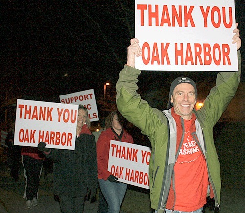 Oak Harbor High School art teacher Frank Jacques waves a sign on Highway 20 with a crowd of teachers walking toward the intersection with Whidbey Avenue Monday night.