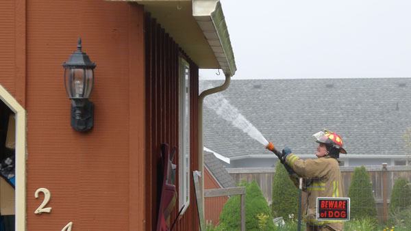 A firefighter hoses down a small fire that started in a storage room adjacent to a garage at a North Whidbey home Friday.