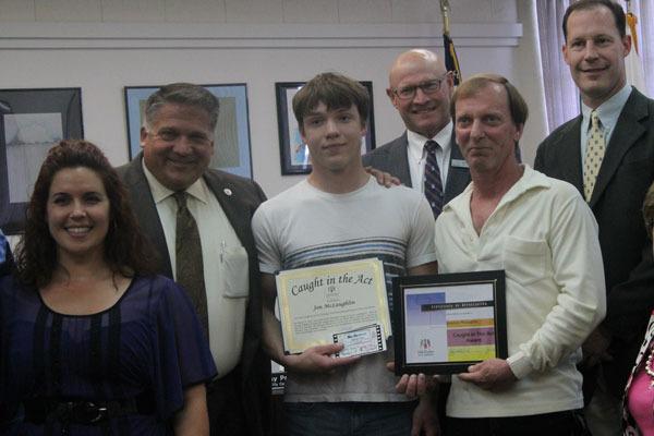 Jonathan McLaughlin stands with his father and city officials after receiving the Caught in the Act award.