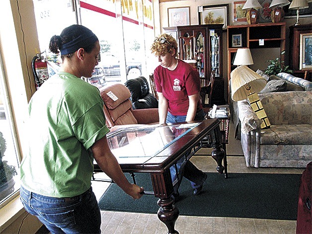 Active-duty Navy volunteers Kaelyn Hall and Jenna Sowers arrange showroom furniture.