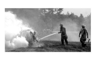 Firefighters douse a hay bale that burned during a brush fire Wednesday afternoon. The fire scorched a field between Oak Harbor and Goldie roads.