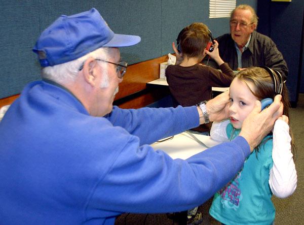 Oak Harbor Lions Club member Jim Ryan helps Crescent Harbor Elementary School kindergarten student Kelsey Bull into headphones for a hearing test.