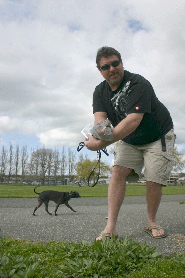 Dog walker Remi Chabot cleans up after his dog in Windjammer Park. Dog walkers are required to carry waste bags. Disposal cans are located in various places in Windjammer Park and on the Scenic Heights Trail.