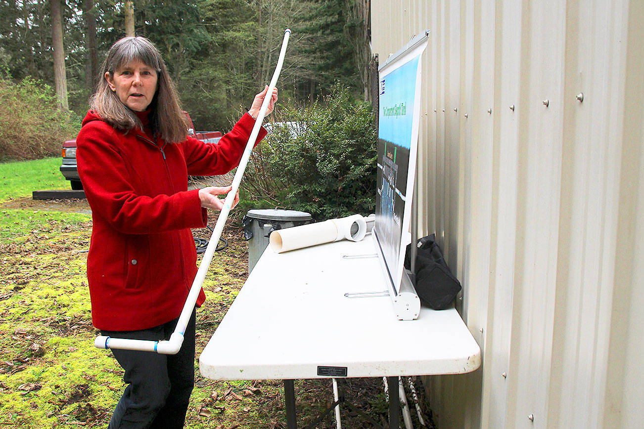 Photo by Patricia Guthrie/Whidbey News-Times                                Island County environmental health inspector Maribeth Crandell demonstrates a sludge stick used to measure accmulation in a septic tank. The above ground concrete tank and exposed pipes are used for education. Crandell begins teaching septic system safety to the public this month.