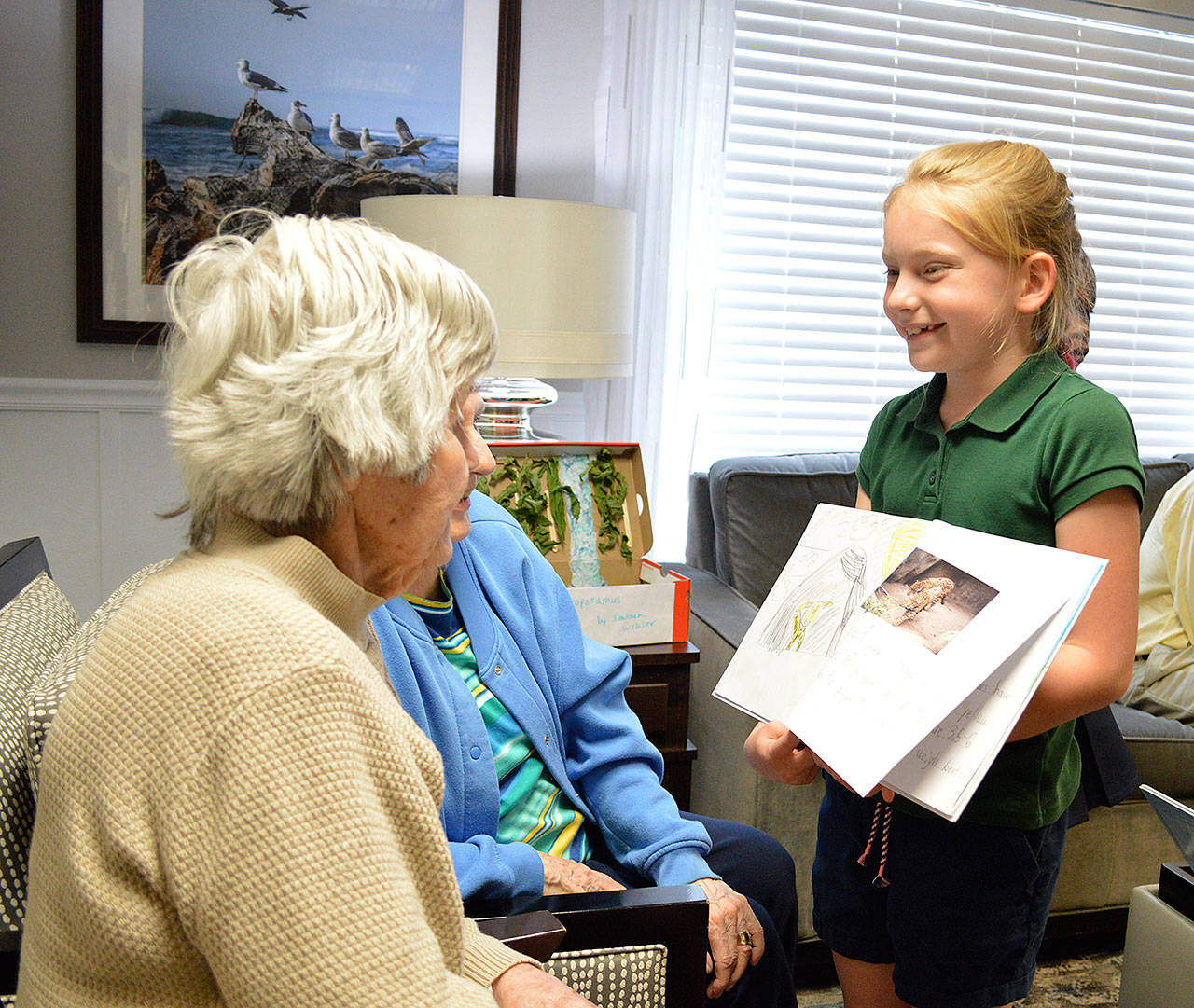 Olive Porter (foreground) and Phyllis Rollag listen to second-grader Lucy Baker read the book she created about jaguars at Regency on Whidbey. Second-grade students at Oak Harbor Elementary School picked animals at the Woodland Park Zoo in Seattle, researched them and created hard-cover books and dioramas, which they shared with Regency residents Wednesday. Photo by Laura Guido/Whidbey News-Times