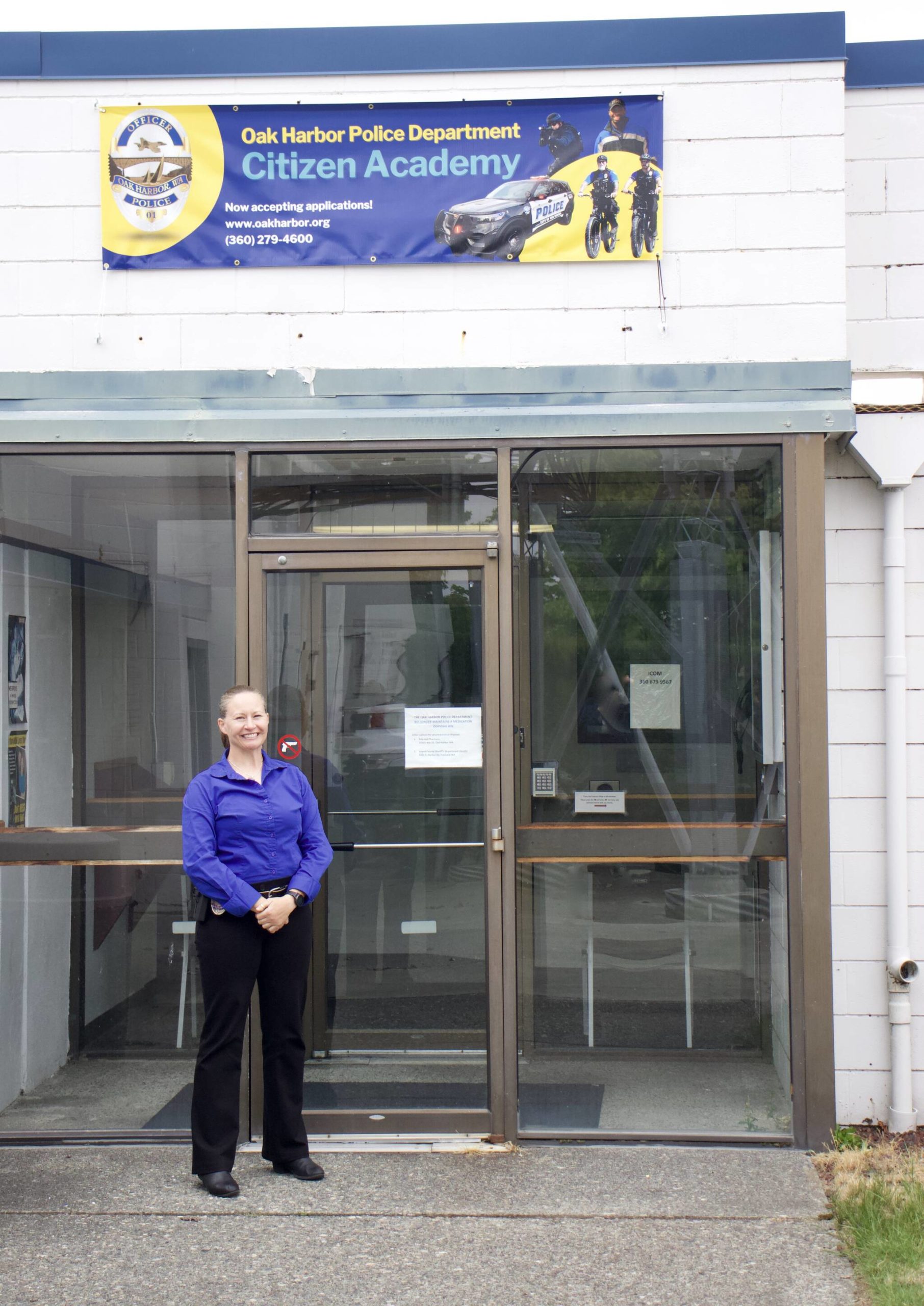 Detective Sgt. Jennifer Gravel stands under the banner advertising Citizen Academy. (Photo by Rachel Rosen/Whidbey News-Times)