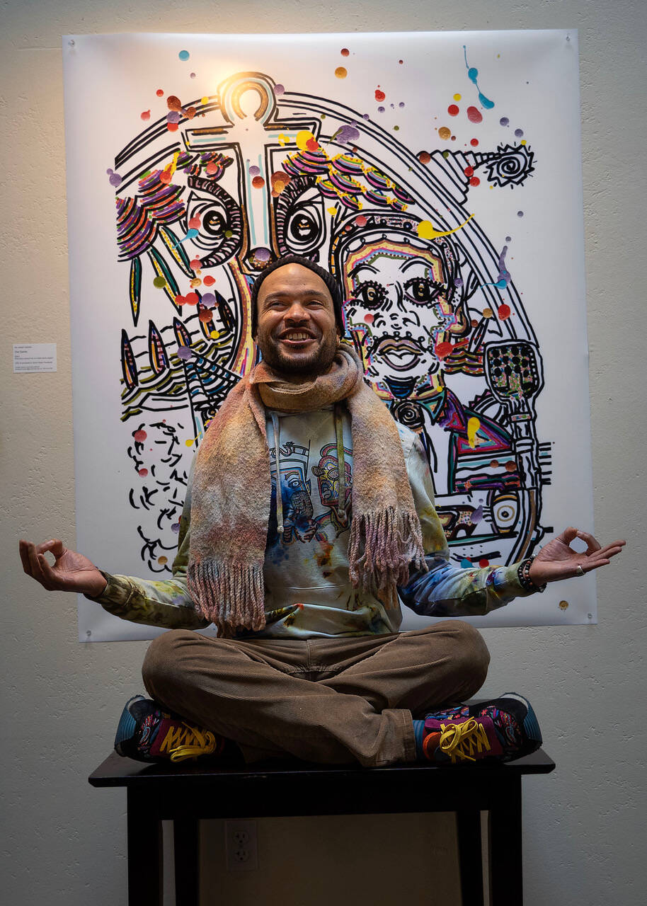 Photo by David Welton
Dressed in brightly tie-dyed clothing he made himself, Ian Joseph Jackson strikes a meditative pose in front of his artwork that includes Martin Luther King Jr. at the podium.