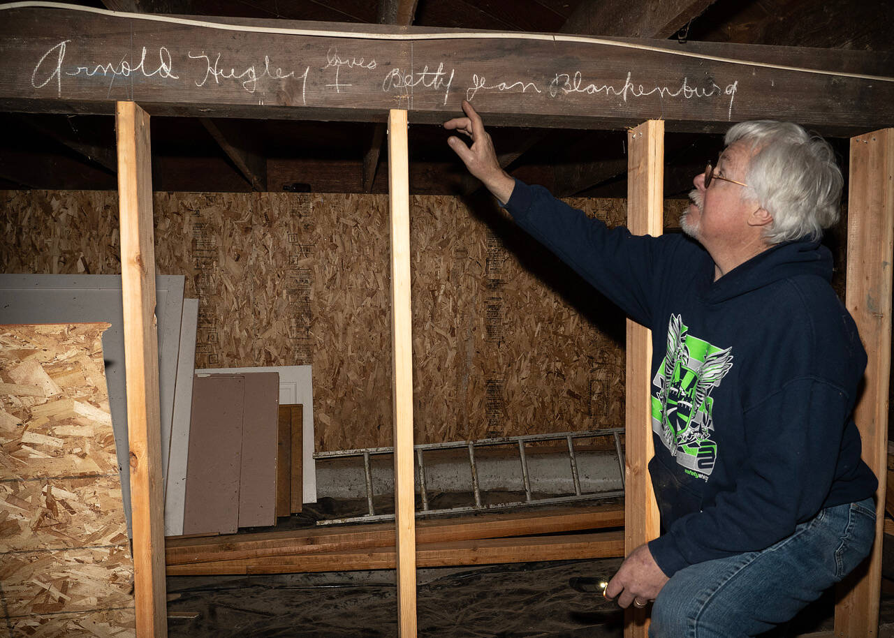 Holmes Harbor Activity Club President Andy Campbell points out the chalked phrase beneath Freeland Hall, “Arnold Hugley loves Betty Jean Blankenburg.” The building’s crawl space has many other affirmations of love written throughout it, which likely date back to the 1940s. (Photo by David Welton)