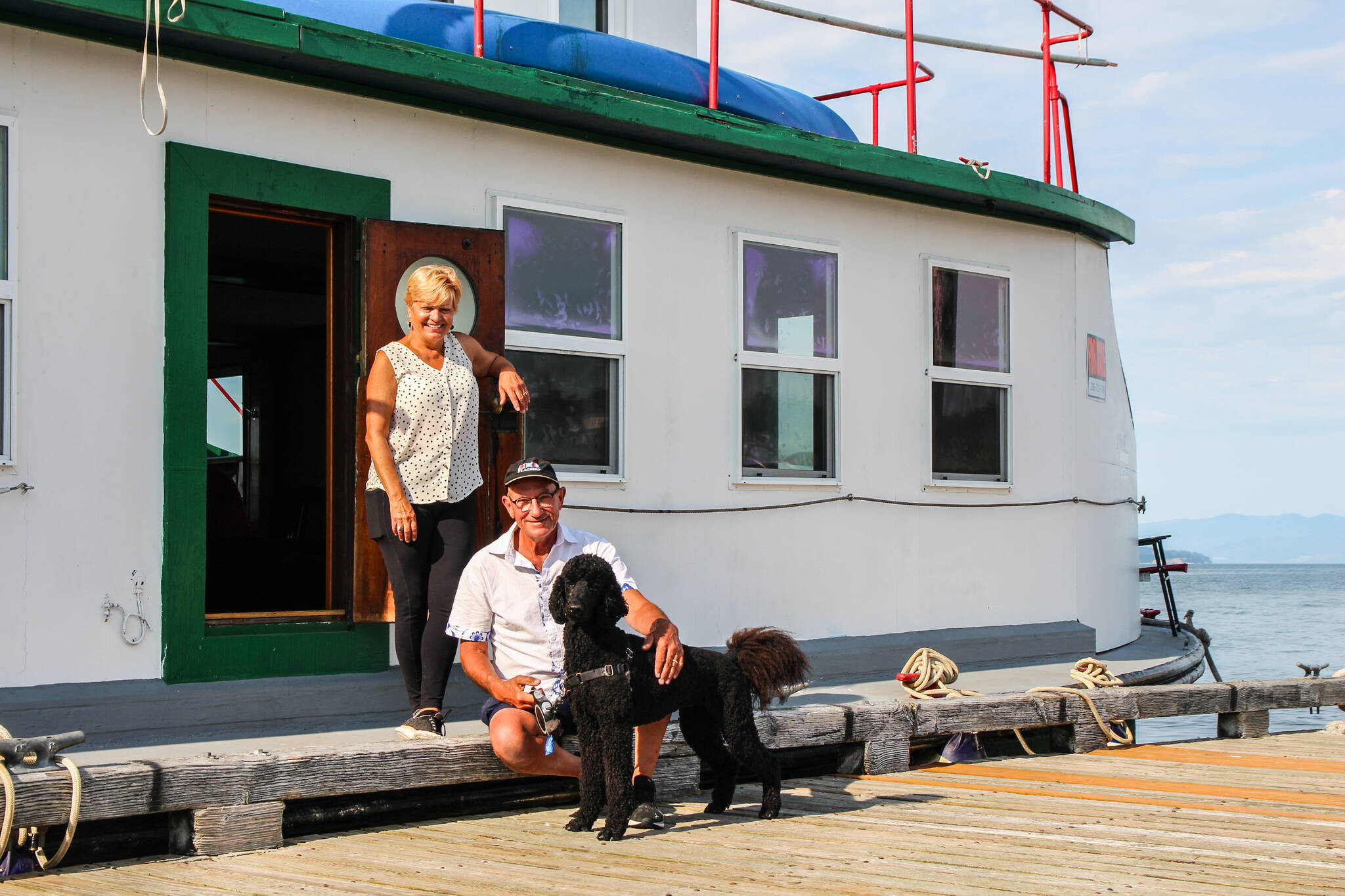 Kat and Dennis Redmon smile in front of their ferry house with their dog, Gigi. (Photo by Luisa Loi)