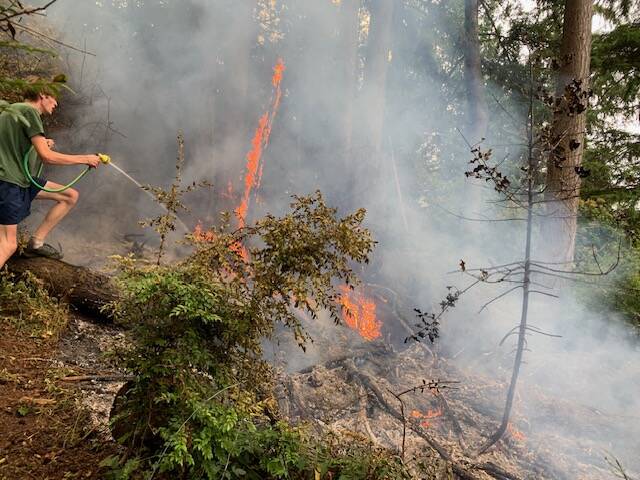 Hillel Coates mans a garden hose to fight a brush fire. (Photo by John Graham)