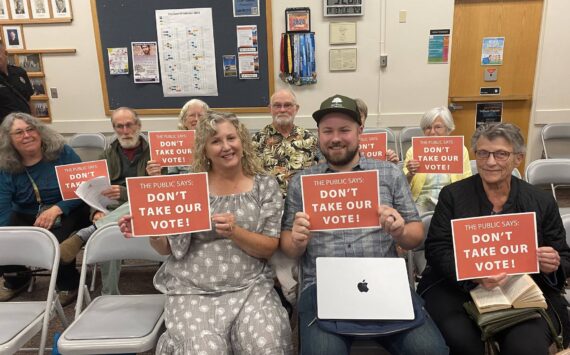 Members of the Whidbey Environmental Action Network, Garry Oak Society and Whidbey community hold "Don't take our vote!" signs at the Aug. 13 Oak Harbor city council meeting. (Photo by Amanda Bullis)